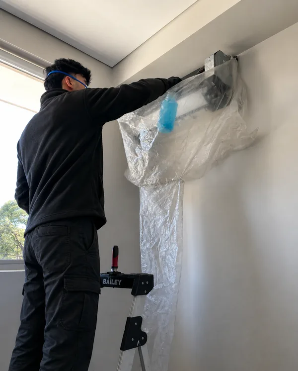 Bendigo aircon cleaner preparing a wall-mounted split-system air conditioner for cleaning with a protective cover